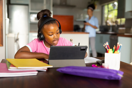 Happy african american daughter in headphones having online lesson using tablet at home