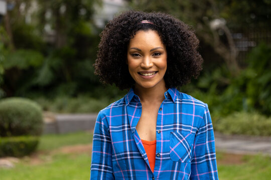 Portrait of happy african american woman wearing plaid shirt smiling in garden