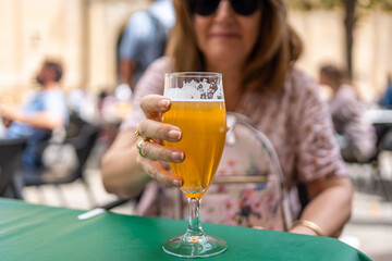Glass of beer held by the hand of a woman on a terrace of a bar on the street, Spain.