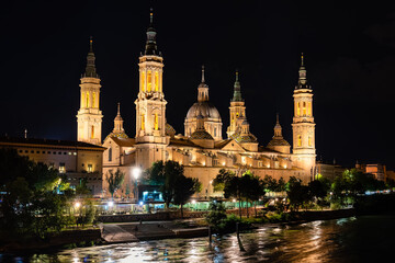 Fototapeta na wymiar Cathedral basilica of the Pilar of Zaragoza illuminated at night next to the river Ebro, Spain.