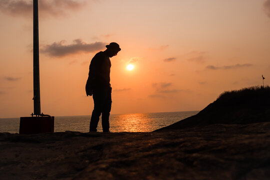 the silhouette image of a sad boy standing near an ocean with sun in the background