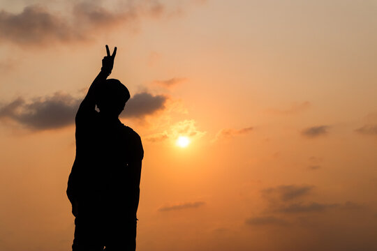 the silhouette image of a boy showing winning gesture with sky in the background