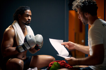 Muscular and strong boxing player in sweats after workout, resting on bench face to face with his...