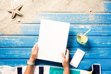 Woman hands holding white blank magazine cover mockup on beach towel
