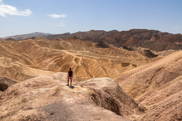 Fototapeta na wymiar Man with scenic view Badlands of Zabriskie Point, Furnace creek, Death Valley National Park, California, USA. Erosional landscape of multi hued Amargosa Chaos rock formations, Panamint Range in back
