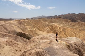 Man with scenic view Badlands of Zabriskie Point, Furnace creek, Death Valley National Park, California, USA. Erosional landscape of multi hued Amargosa Chaos rock formations, Panamint Range in back