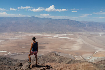 Fototapeta premium Rear view of man overlooking the Salt Badwater Basin and Panamint Mountains seen from Dante's View in Death Valley National Park, California, USA, America. Aerial scenic view on dry desert landscape