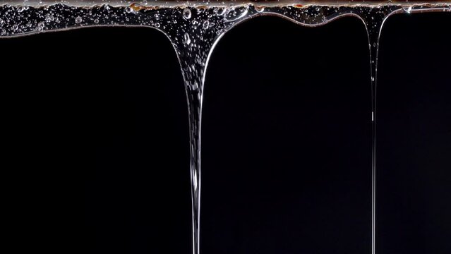 Closeup shot of transparent cosmetic gel fluid flowing on black background.
