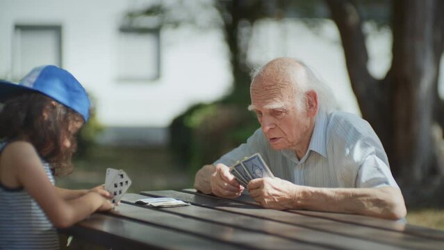 Kind Opa taught his grandson how to play cards in the city park, Close up dolly shot
