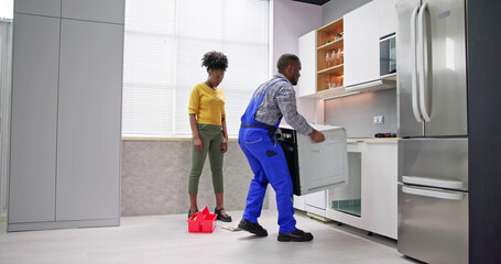 Young Woman Looking At Male Worker In Overall Repairing Oven