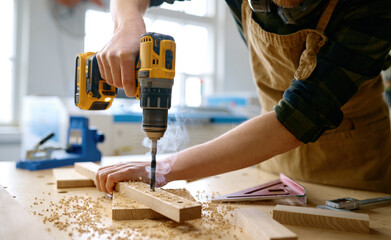 Carpenter working with drill leaning over table at carpentry workshop