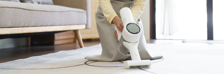 Maid using handheld cordless vacuum cleaner to vacuuming and cleaning the dust on carpet in home