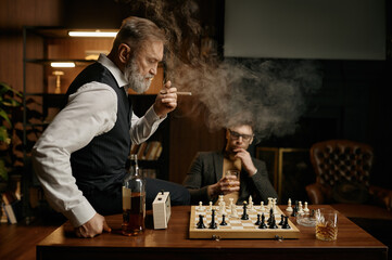 Two chess players taking break for smoking cigar and planning strategy of game
