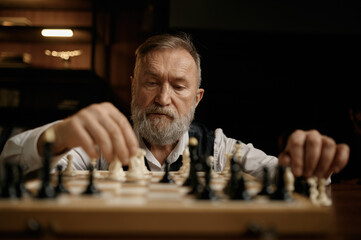 Face portrait of senior man moving chess piece on board during competition match