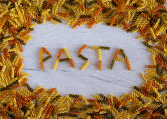 The word pasta is laid out of fusilli pasta on a white wooden background on pasta frame