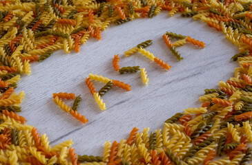 Fototapeta na wymiar The word pasta is laid out of fusilli pasta on a white wooden background on pasta frame