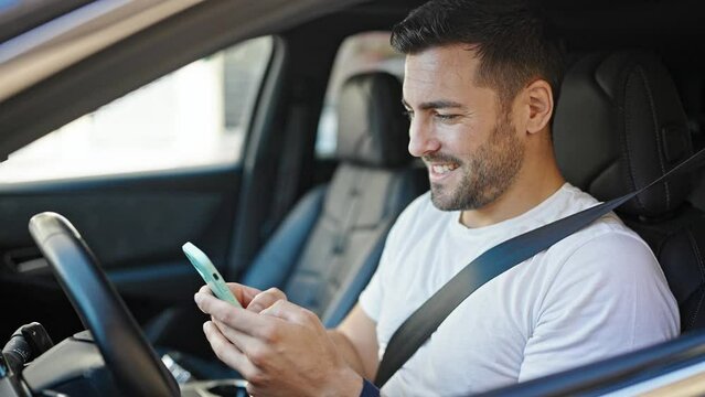 Young hispanic man using smartphone sitting on car at street