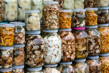 Pickled mushrooms (chanterelles, milk mushrooms, porcini mushrooms) in jars on the counter. Small home business. Own production.