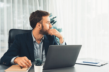 Businessman in black suit working on laptop at his workspace desk. Smart executive researching financial data and planning marketing strategy on corporate laptop at modern workplace. Entity