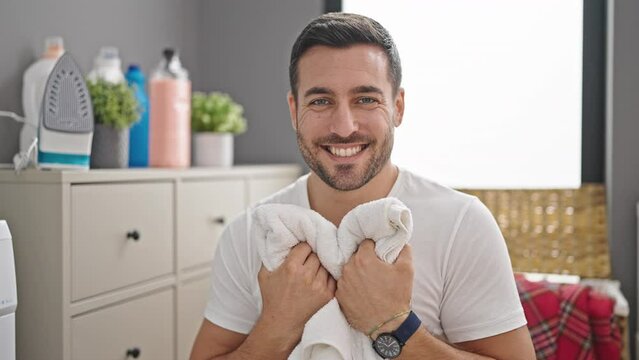 Young hispanic man smiling confident smelling clothes at laundry room