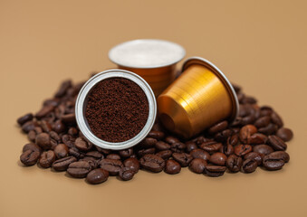 Capsules with ground coffee on fresh raw aroma beans on beige background.
