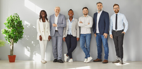 Happy multicultural business people standing in row against wall in office. Smiling diverse corporate team posing differently looking at camera. Multiethnic corporate staff, HR agency recruitments