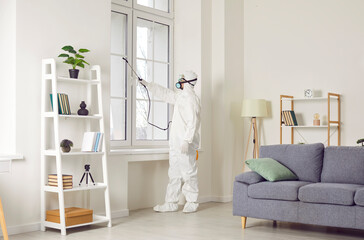 Service man wearing protective ppe suit, glasses and face mask disinfecting flat during pandemic or doing pest control with disinfectant spray. Home disinfection and protection concept.