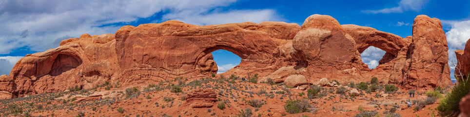 Panoramic view of North Window, South Window, and Turret Arch with beautiful clouds in the sky, small figures of people in the frame emphasize the scale and beauty of this majestic creation, Moab, USA © underwaterstas