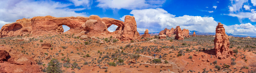 Fototapeta premium Panoramic view of North Window, South Window, and Turret Arch with beautiful clouds in the sky, small figures of people in the frame emphasize the scale and beauty of this majestic creation, Moab, USA