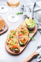 Gourmet lunch with avocado salmon toasts on rye bread and rose wine glasses, gray table background, top view