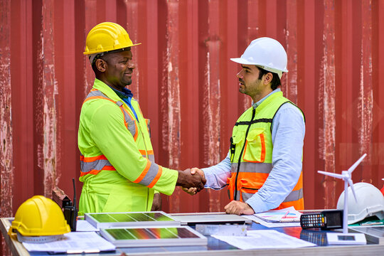 Engineer and African american foreman shake hand for start working with solar cell and container box site.
