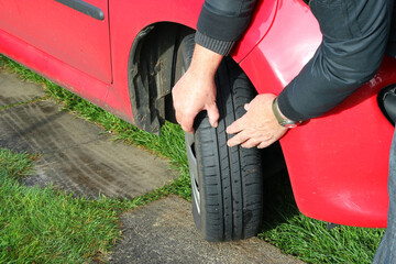 Man inspecting his car tire or tyre by feeling the depth of the tread.