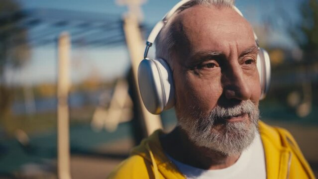 Active senior man putting on headphones to listen to music at the sport ground