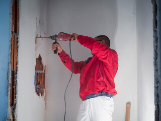 Home renovation. Portrait of worker in red workwear drilling wall with hammer drill. Destroying...