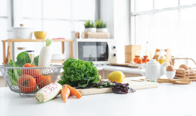 Focus on fresh green vegetable in home kitchen, yellow lemon placed on cutting board, carrots, corn, tomatoes, white radish, cos salad in basket, Eggs, seasoning in blur background. Healthy food