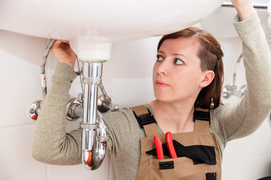 female plumber repairs or installs pipes under a sink