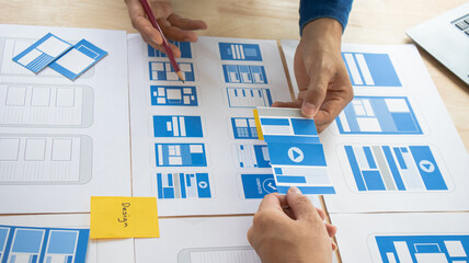 Close-up ux developers and ui designers use augmented reality to brainstorm on mobile app interface wireframe designs on modern office desks. Creative digital development office