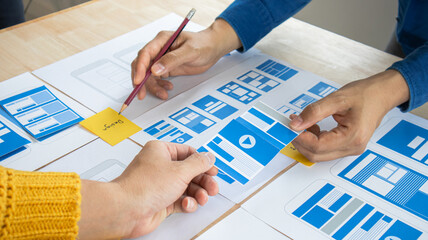 Close-up ux developers and ui designers use augmented reality to brainstorm on mobile app interface wireframe designs on modern office desks. Creative digital development office