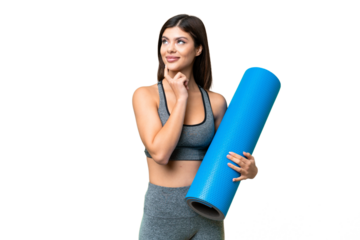 Young sport woman going to yoga classes while holding a mat over isolated chroma key background thinking an idea while looking up
