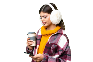 Young Russian woman wearing winter muffs over isolated chroma key background holding coffee to take away and a mobile