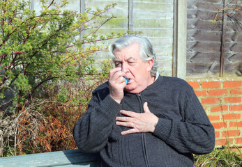 Senior or elderly man having difficulty breathing and using an inhaler.  Asthma or chest infection.