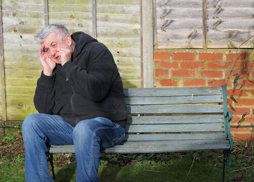Senior or elderly man suffering from stress and anxiety. Sitting on a bench and having a panic attack.