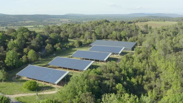 Aerial shot in rotation that rises above a farm of solar panels to reveal the wooded countryside