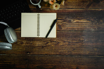 Top view of blank spiral notepad, pen, headphone and coffee cup on wooden table