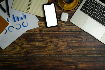 Smartphone with blank screen, laptop, notepad and financial documents on wooden working desk. Flat lay, Top view with copy space