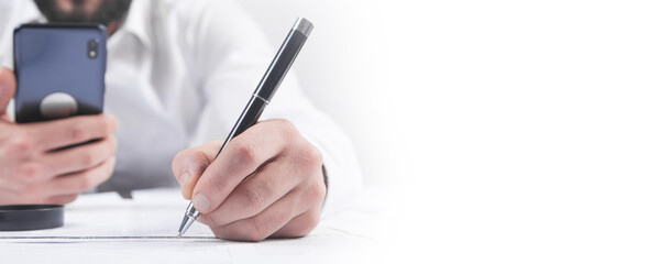 Businessman signing contract and using smartphone in office.