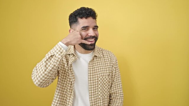 Young hispanic man smiling confident doing call me gesture with hand over isolated yellow background