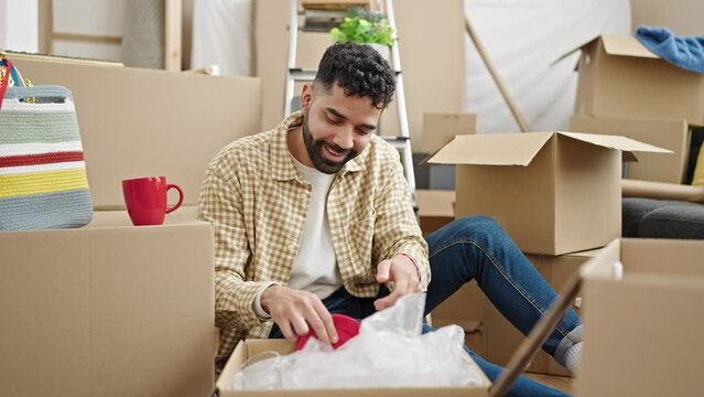 Young hispanic man unpacking cardboard box at new home