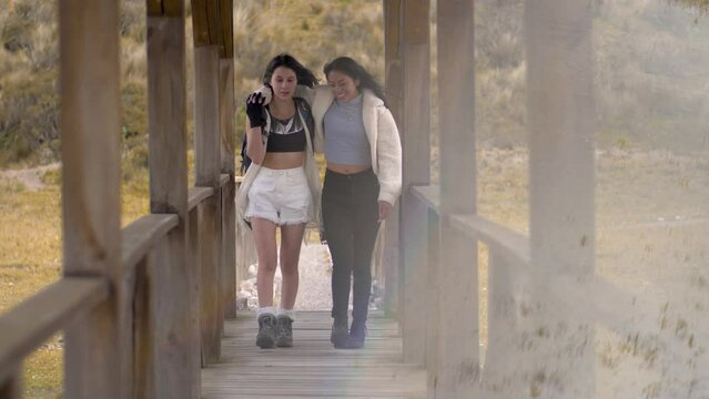 Two athletic woman hikers walk along wooden bridge, wind blows hair