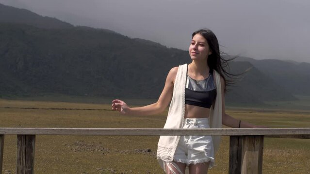 Girl in black crop top and white cardigan adjusts hair blowing in wind at cotopaxi national park